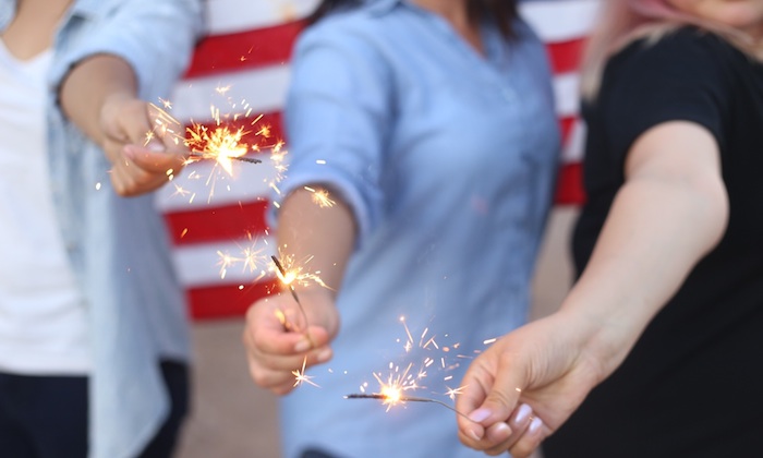 girls holding sparklers in front of american flag