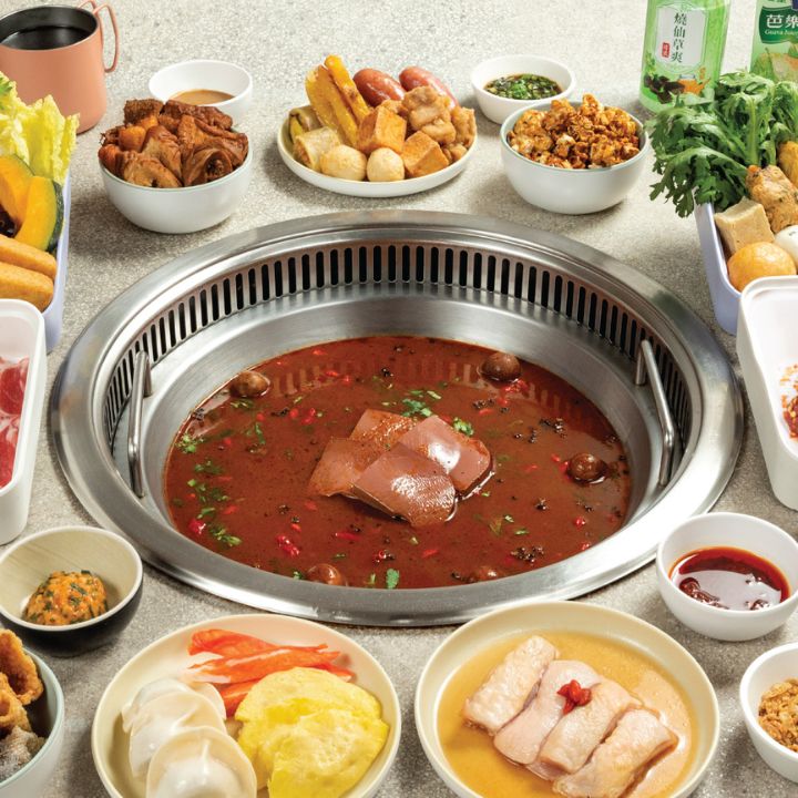 Shabu shabu soup in stainless steel pot, surrounded by vegetables, tofu, noodles and condiments in white tableware.