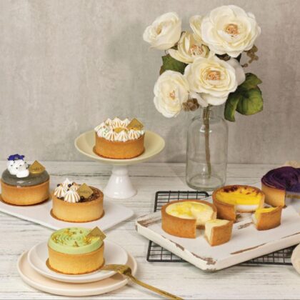 Assortment of whole and cut lemon, fruit and custard tarts served on white porcelain platters, with roses in a clear vase.